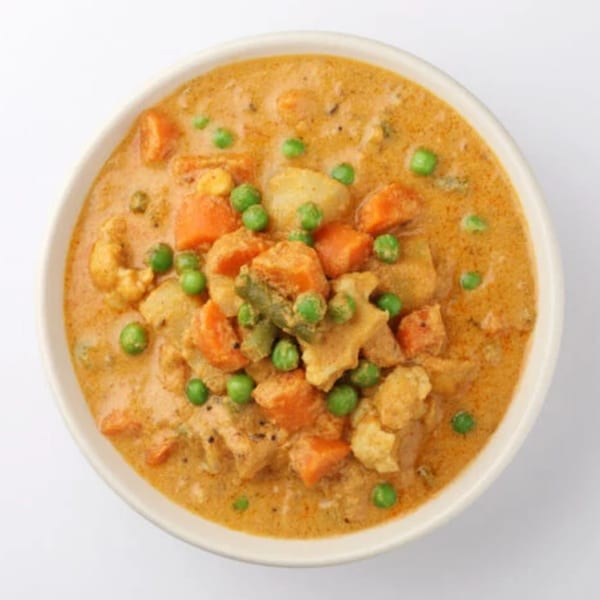 A bowl of Indian vegetable curry with carrots, peas, and potatoes in a creamy orange sauce.