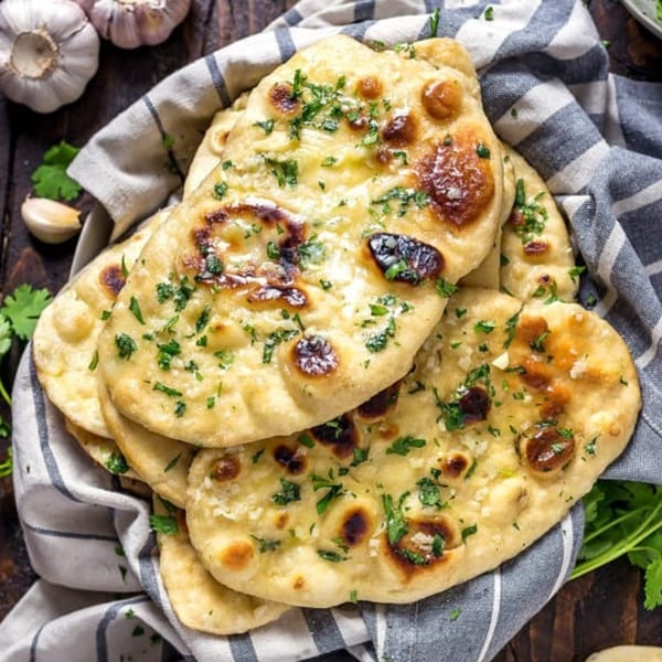 Golden-brown garlic naan bread, garnished with fresh cilantro, served in a striped cloth.