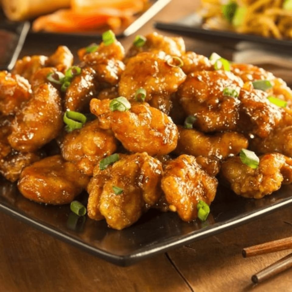 A plate of golden-brown General Tso's chicken, garnished with chopped green onions.