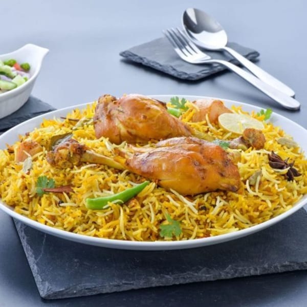 A large white bowl of chicken biryani with two chicken drumsticks, rice, and spices.