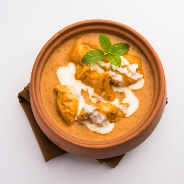 Indian butter chicken in a terracotta bowl, garnished with cream and mint leaves.